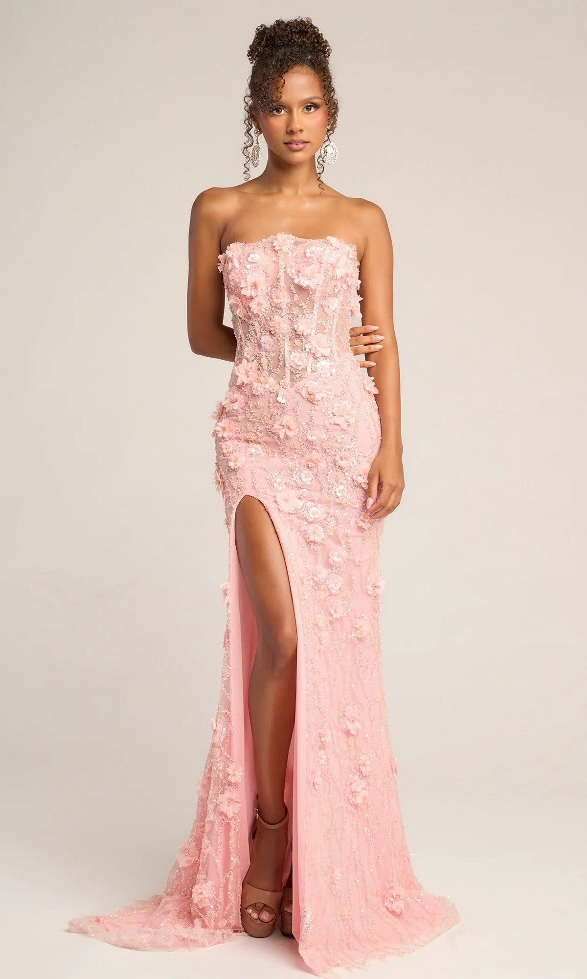 A woman models the Portia and Scarlett PS26011, a blush pink strapless long formal dress with 3D floral details and a thigh-high leg slit, set against a plain background.